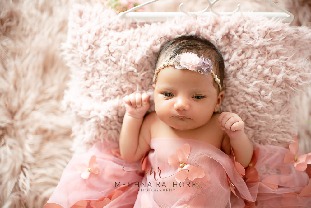 24 days old newborn girl child wearing a pink dress and smiling while lying on a bed in best indoor photo studio at meghna rathore photography in gurgaoun